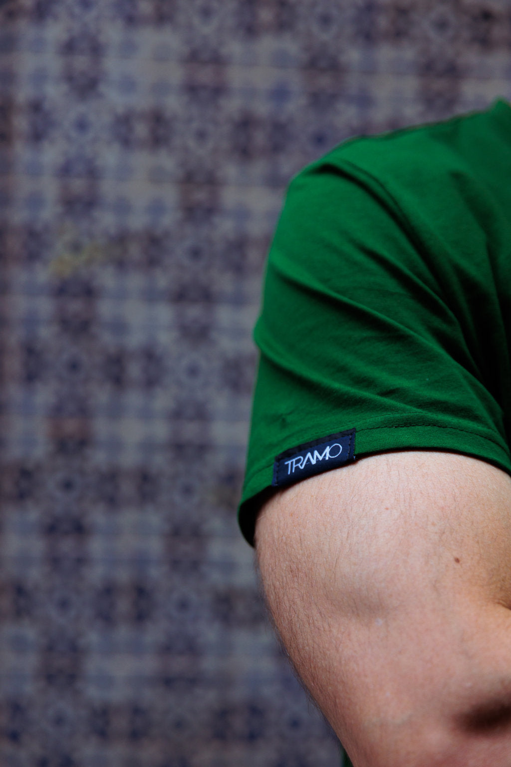 Detalle de la etiqueta de TRAMO cosida en la manga de una camiseta verde de algodón.