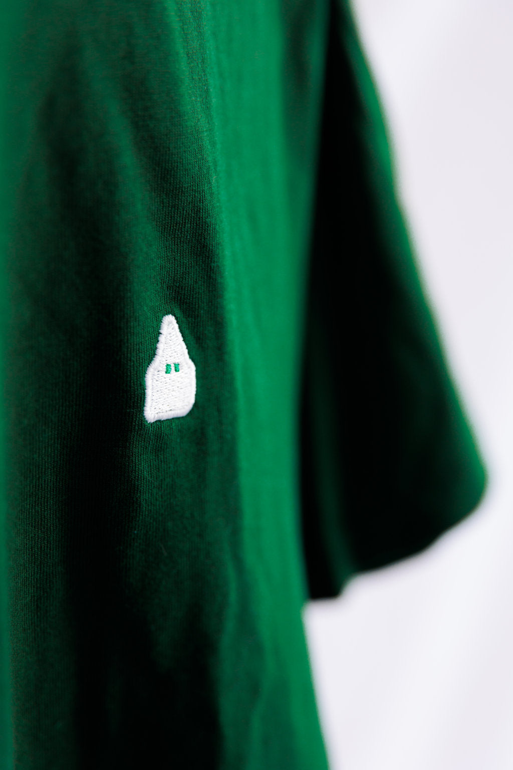 Detalle del nazareno de TRAMO bordado en blanco sobre camiseta verde de algodón.