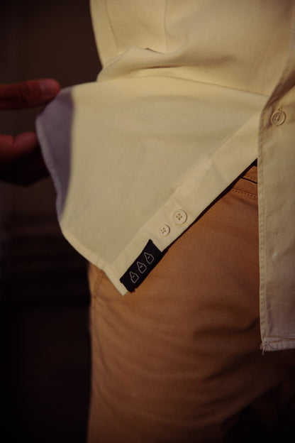 Detalle de la etiqueta TRAMO en la parte inferior de la abotonadura de una camisa crema de algodón