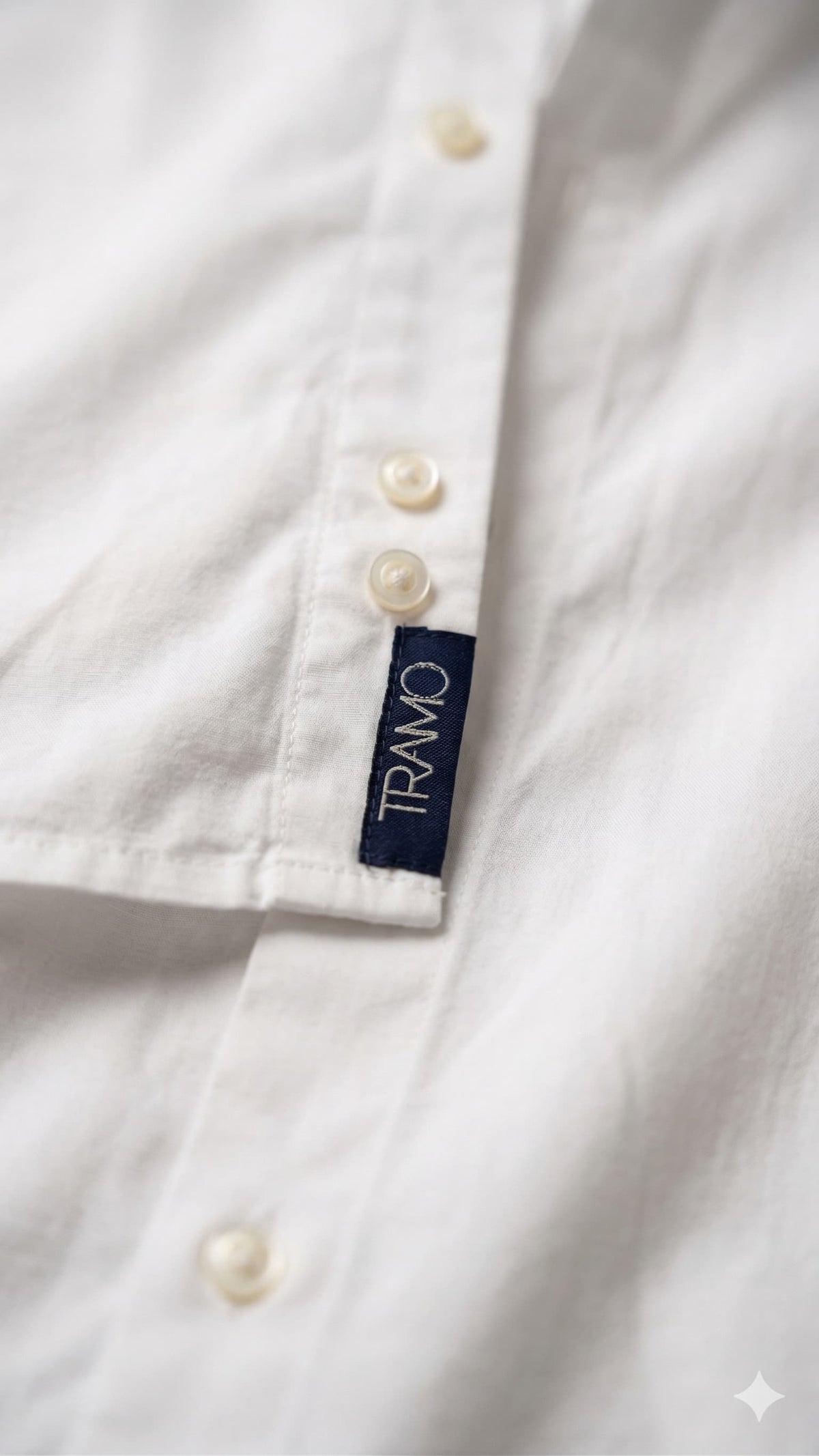 Detalle de la etiqueta TRAMO en la parte inferior de la abotonadura de una camisa blanca de algodón