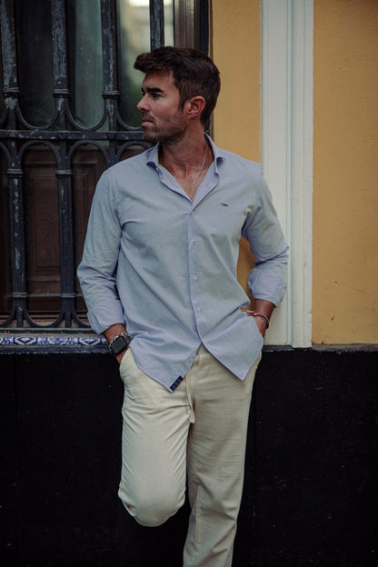 Hombre vistiendo camisa celeste de algodón TRAMO y pantalón chino claro en un espacio exterior
