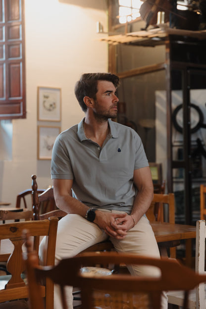 Hombre vistiendo polo gris de algodón TRAMO combinado con pantalón crema en un espacio interior.