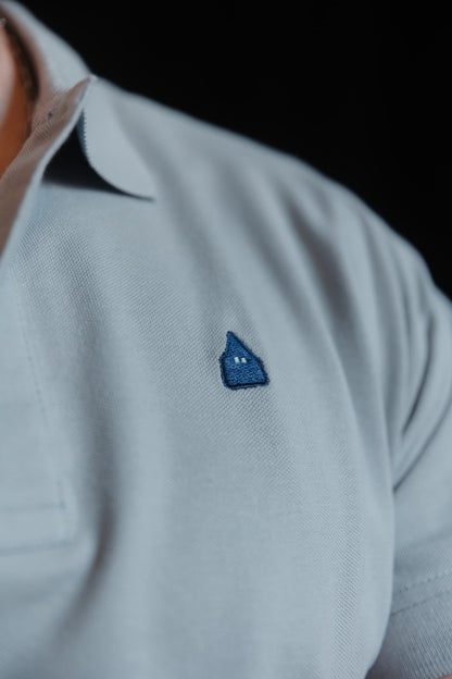 Detalle del nazareno bordado en azul marino sobre polo gris de algodón TRAMO.