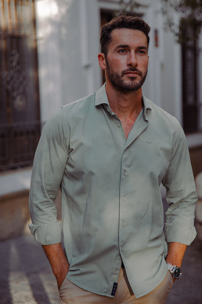 Hombre vistiendo camisa verde de algodón TRAMO, cuello italiano y pantalón chino beige en un espacio exterior