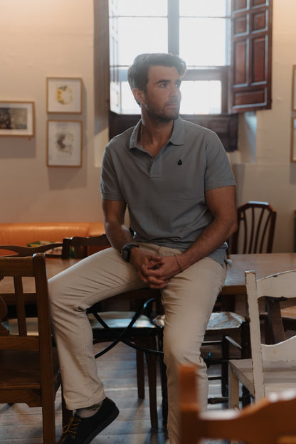 Hombre vistiendo un polo gris de algodón TRAMO con pantalón crema en un espacio interior.