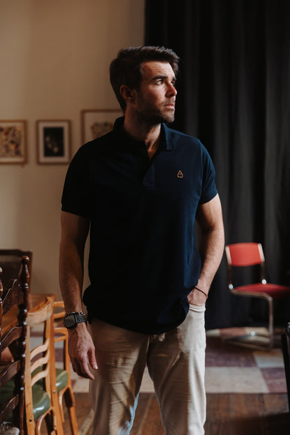 Hombre vistiendo polo azul marino de algodón TRAMO combinado con pantalón beige en un espacio interior.