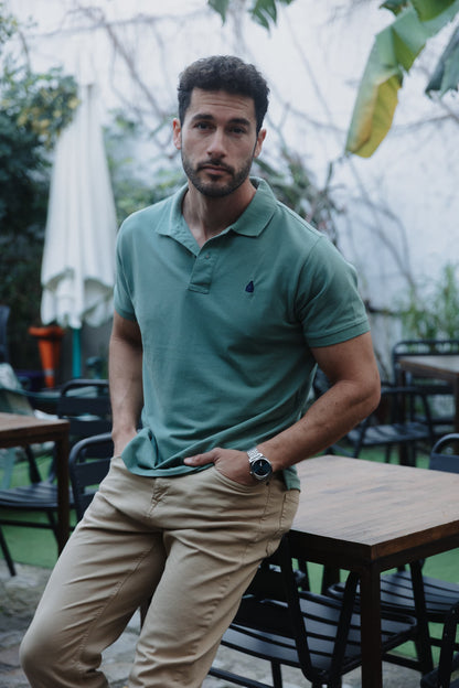 Hombre con polo verde de algodón TRAMO combinado con pantalón beige en una terraza exterior.