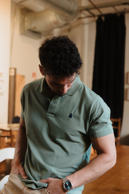 Primer plano de hombre con polo verde TRAMO de algodón, cuello clásico y nazareno bordado en azul marino.