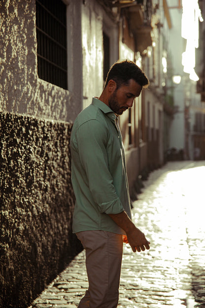 Hombre vistiendo camisa verde de algodón TRAMO de manga larga y pantalón chino beige en un espacio exterior