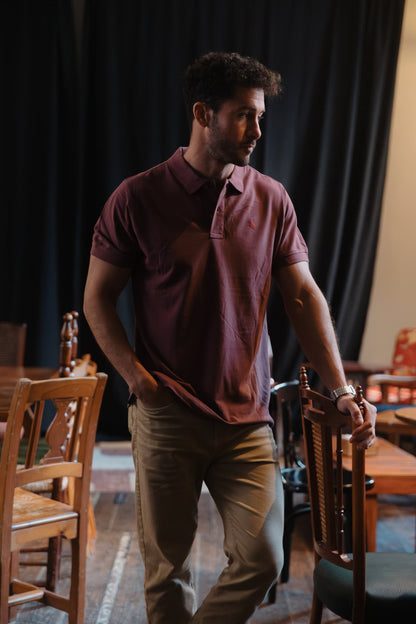 Perfil de hombre con polo burdeos de algodón TRAMO combinado con pantalón beige en un espacio interior.